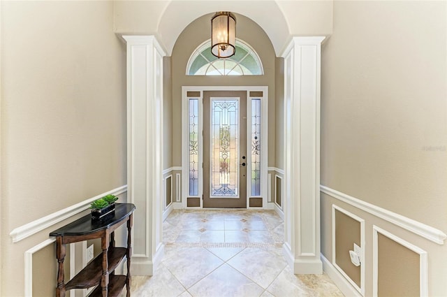 foyer entrance with ornate columns, arched walkways, a decorative wall, and light tile patterned floors