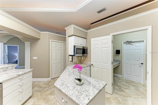 kitchen featuring ornamental molding, stainless steel microwave, light stone countertops, and visible vents