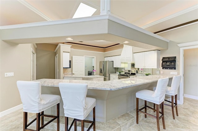 kitchen featuring a peninsula, light stone countertops, a breakfast bar, white cabinets, and stainless steel appliances