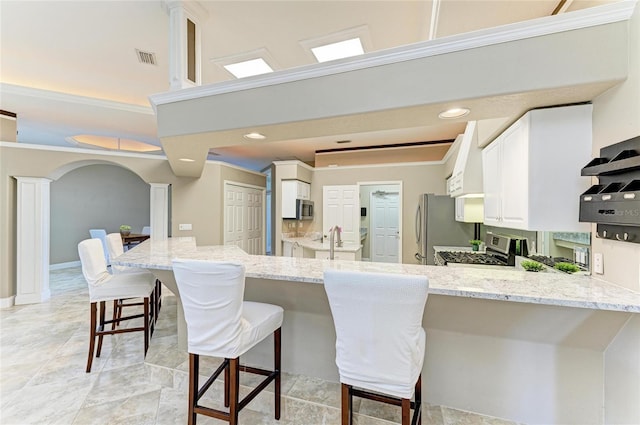 kitchen with a peninsula, light stone countertops, appliances with stainless steel finishes, and a breakfast bar