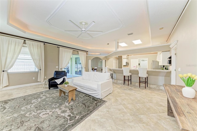 living area featuring arched walkways, ceiling fan, a healthy amount of sunlight, and a raised ceiling