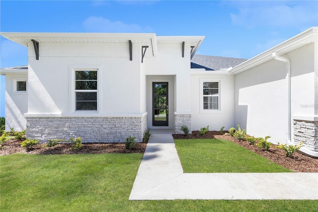 view of front of home featuring a front yard, a shingled roof, stone siding, and stucco siding