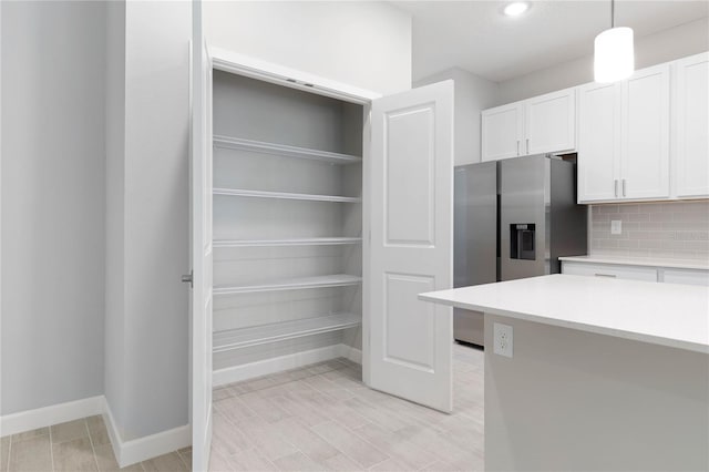 kitchen with stainless steel fridge with ice dispenser, baseboards, light countertops, white cabinets, and tasteful backsplash