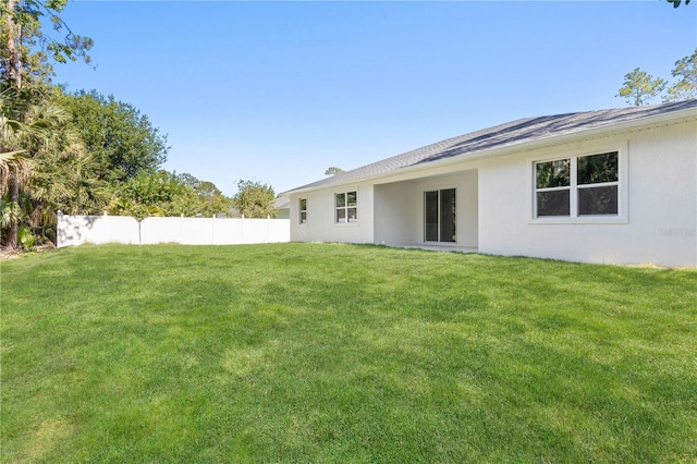 rear view of house with fence, stucco siding, and a lawn