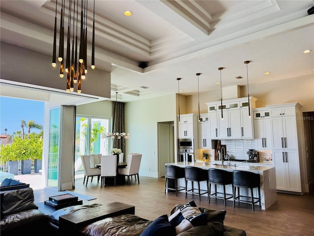 living room with a tray ceiling, recessed lighting, wood finished floors, and a towering ceiling