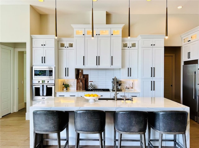 kitchen with a kitchen breakfast bar, a center island with sink, white cabinetry, backsplash, and stainless steel appliances