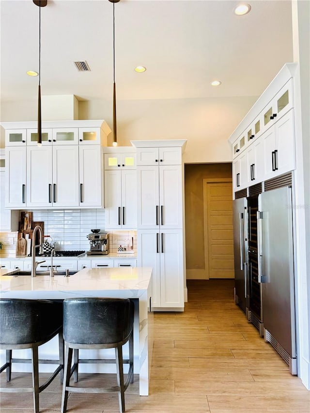 kitchen featuring recessed lighting, light countertops, white cabinets, a sink, and stainless steel built in refrigerator