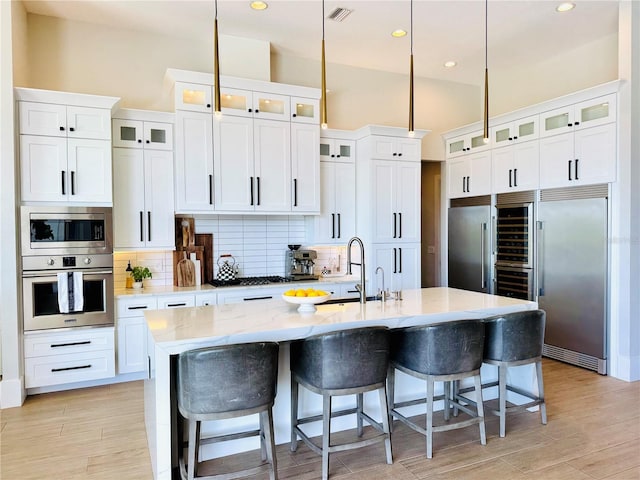 kitchen with visible vents, tasteful backsplash, light wood-type flooring, a sink, and built in appliances