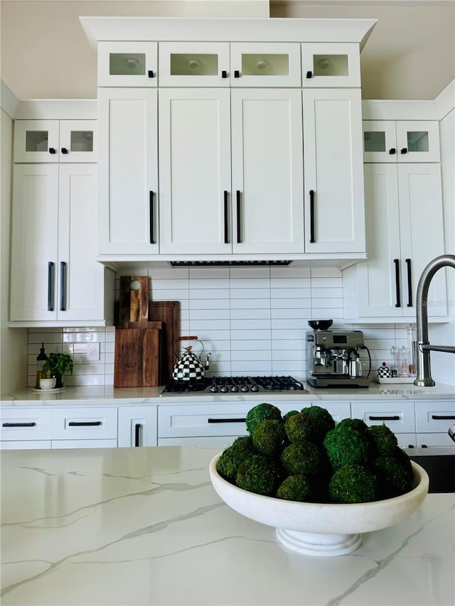 kitchen with glass insert cabinets, tasteful backsplash, light stone countertops, and white cabinets