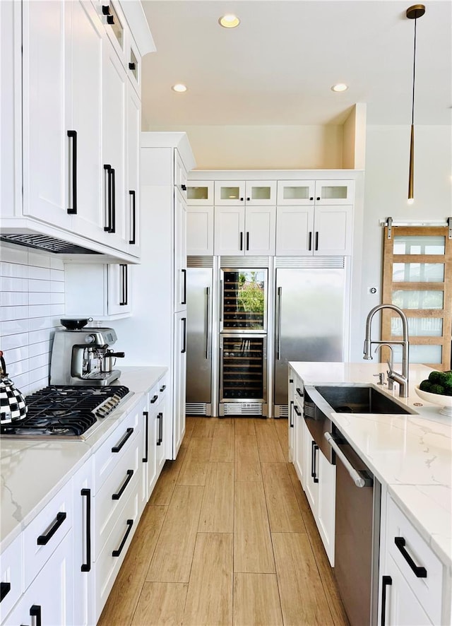 kitchen featuring wine cooler, light wood-type flooring, white cabinets, a sink, and stainless steel appliances