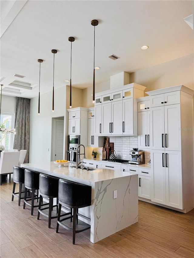 kitchen with visible vents, a kitchen bar, a large island with sink, a sink, and light wood-style flooring