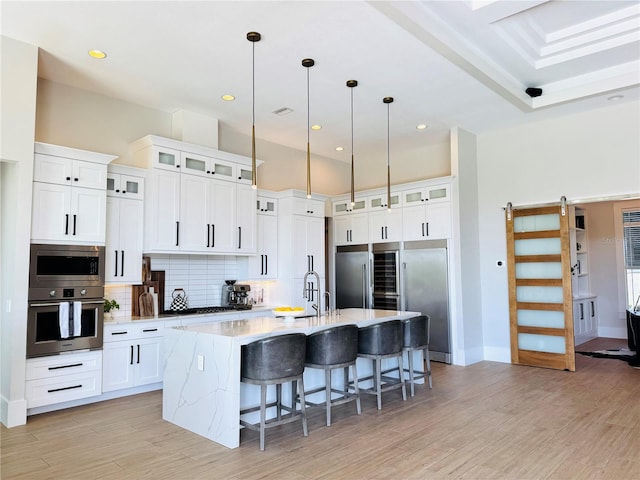 kitchen featuring a kitchen breakfast bar, backsplash, a center island with sink, built in appliances, and light wood-style flooring