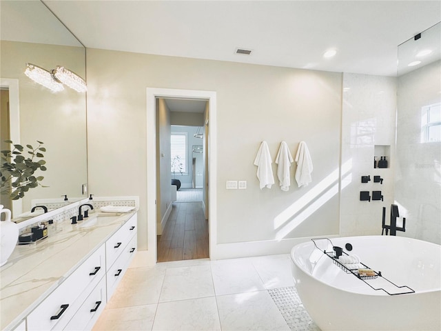 ensuite bathroom featuring baseboards, a healthy amount of sunlight, a soaking tub, and vanity
