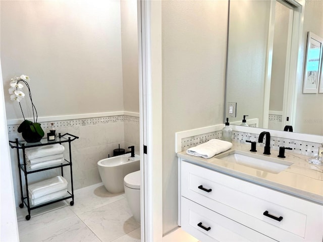 bathroom with vanity, toilet, tile walls, a wainscoted wall, and a bidet