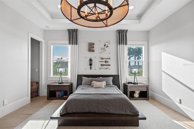 bedroom with an inviting chandelier, a raised ceiling, light wood finished floors, and baseboards