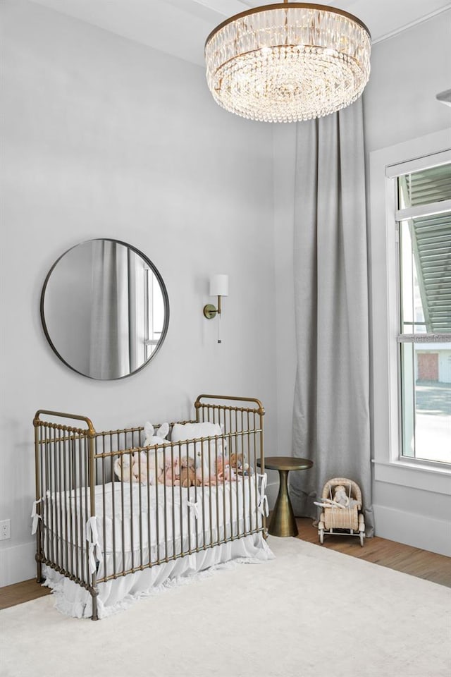 bedroom featuring a nursery area, an inviting chandelier, and wood finished floors