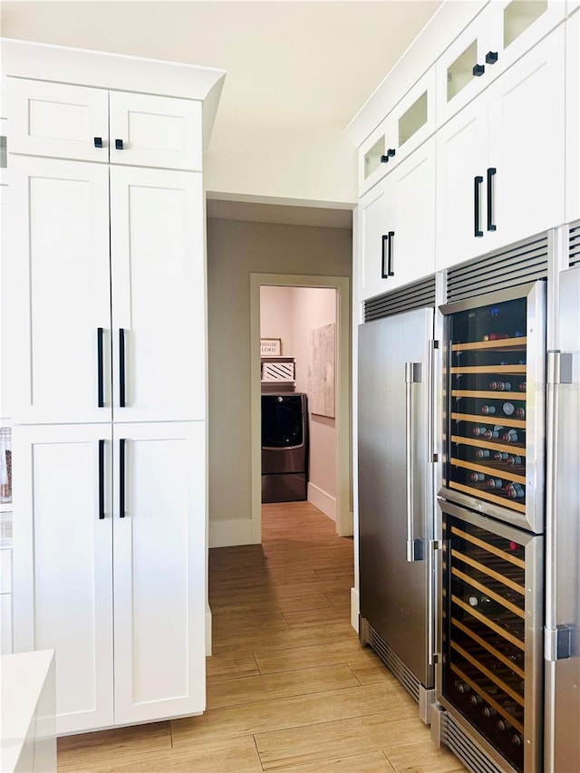 bar featuring light wood-style flooring, washer / clothes dryer, baseboards, wine cooler, and high quality fridge