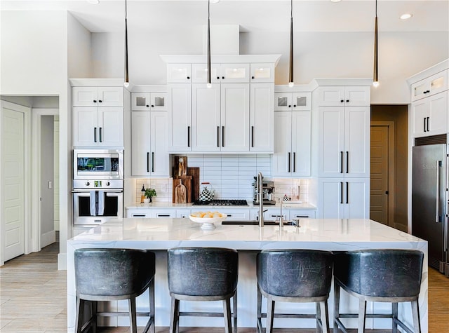 1643 Stanford Ln, Sarasota, FL 34231 - kitchen featuring appliances with stainless steel finishes, white cabinetry, decorative backsplash, a kitchen bar, and a kitchen island with sink