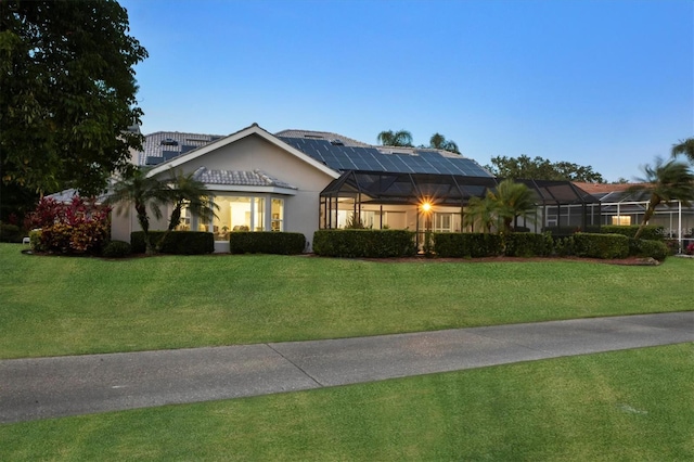 ranch-style house with a lanai, stucco siding, solar panels, and a front lawn