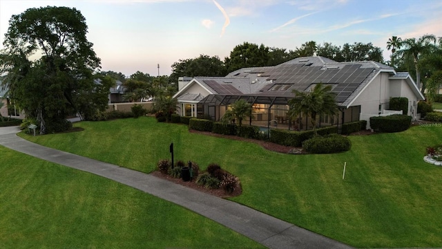 view of front facade with a lawn, solar panels, and glass enclosure