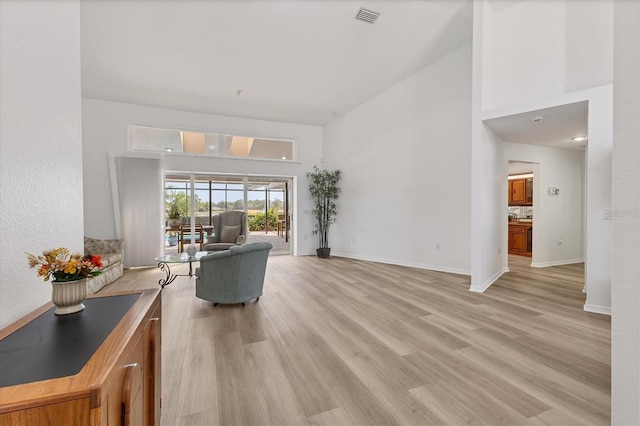 living room featuring visible vents, baseboards, light wood-style flooring, and a high ceiling