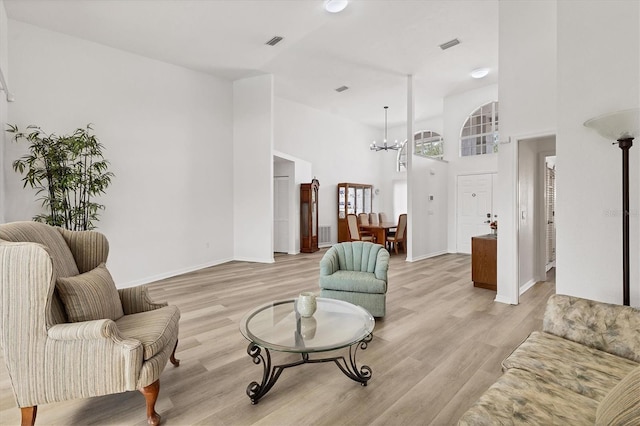living area with light wood finished floors, a chandelier, baseboards, a towering ceiling, and visible vents