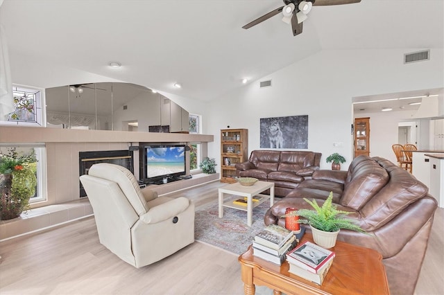 living area featuring light wood-style floors, high vaulted ceiling, ceiling fan, and visible vents
