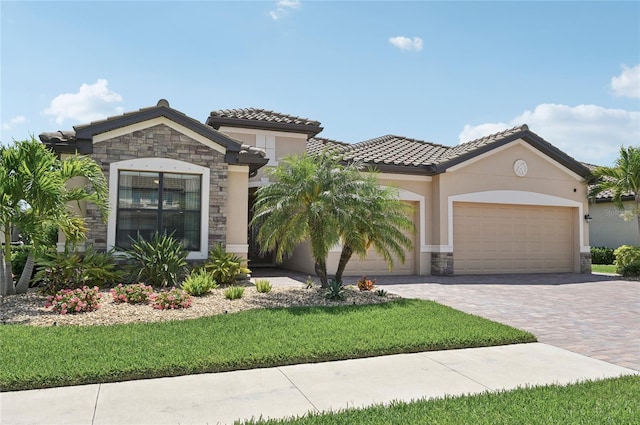 13587 Vancanza Dr, Venice, FL 34293 - mediterranean / spanish-style house featuring an attached garage, a tile roof, stone siding, stucco siding, and decorative driveway