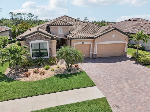 13587 Vancanza Dr, Venice, FL 34293 - mediterranean / spanish-style house featuring a garage, stone siding, decorative driveway, stucco siding, and a tiled roof