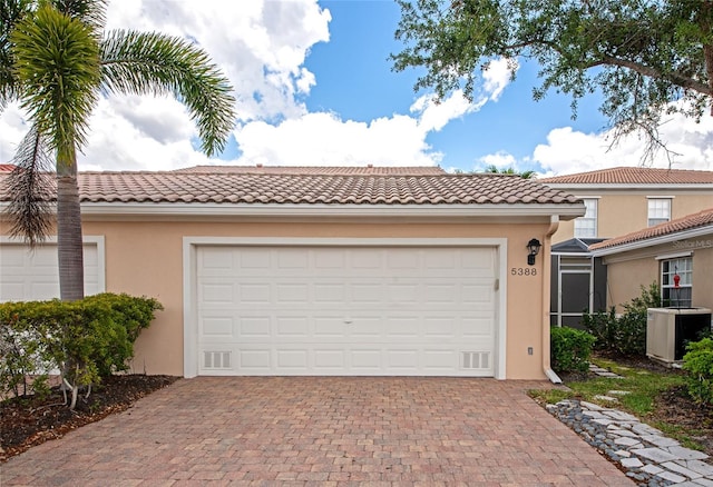 view of front of home featuring a garage, stucco siding, central AC unit, decorative driveway, and a tiled roof