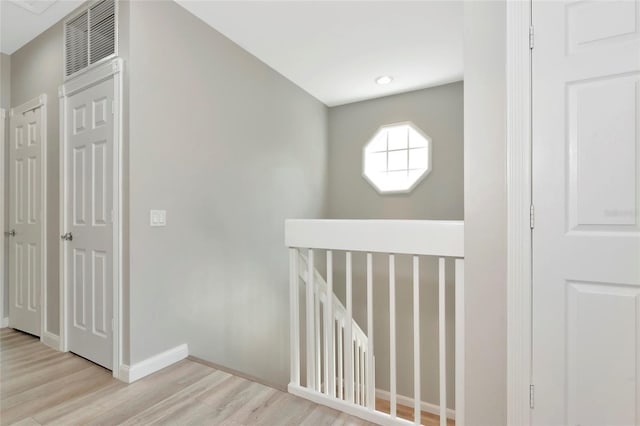 corridor featuring baseboards, visible vents, wood finished floors, and an upstairs landing