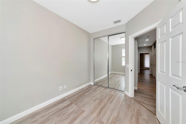 unfurnished bedroom featuring visible vents, light wood-style flooring, baseboards, and a closet