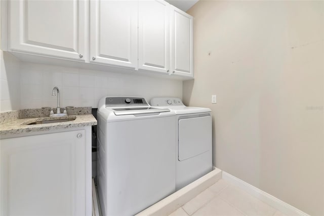 laundry area featuring washer and dryer, light tile patterned flooring, cabinet space, a sink, and baseboards