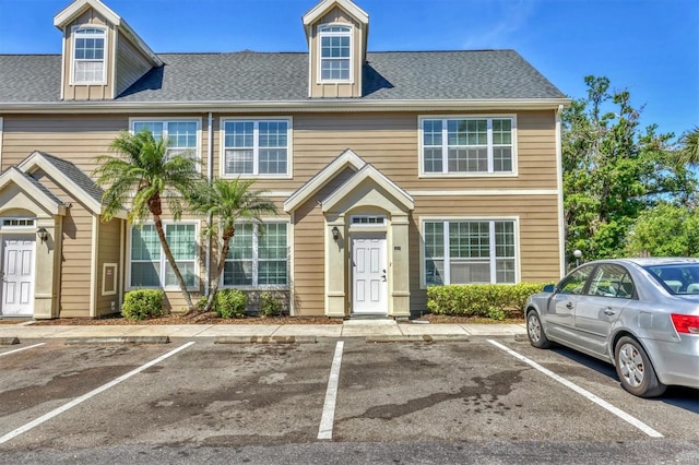view of property with a shingled roof and uncovered parking