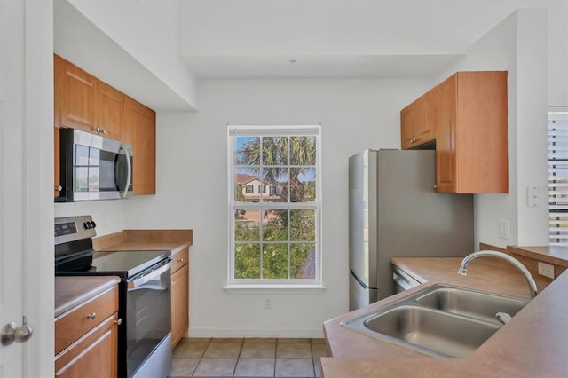 kitchen with a sink, appliances with stainless steel finishes, light tile patterned floors, and a wealth of natural light