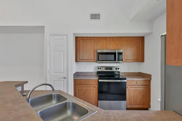 kitchen with brown cabinets, stainless steel appliances, visible vents, and a sink