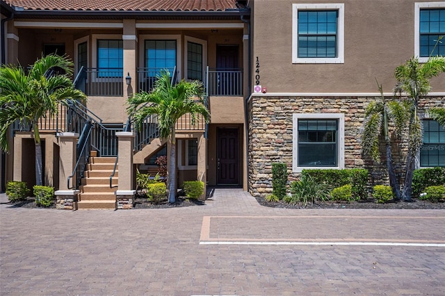 view of front of home with stairs, stone siding, and stucco siding