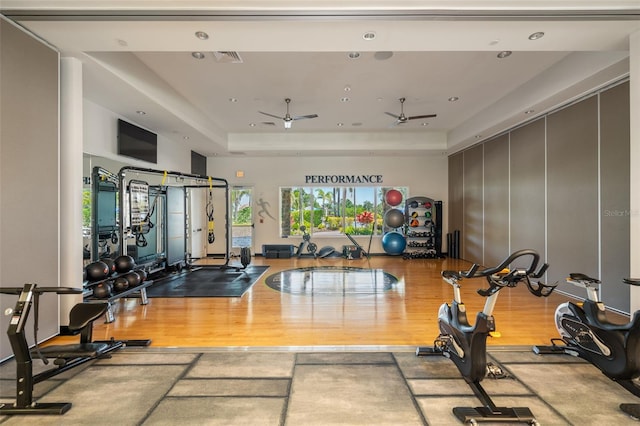 exercise room with visible vents, wood finished floors, recessed lighting, a tray ceiling, and a ceiling fan