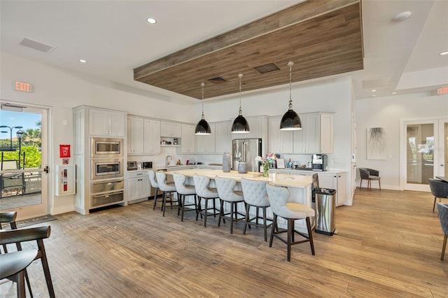 kitchen with an island with sink, a kitchen bar, light countertops, french doors, and appliances with stainless steel finishes