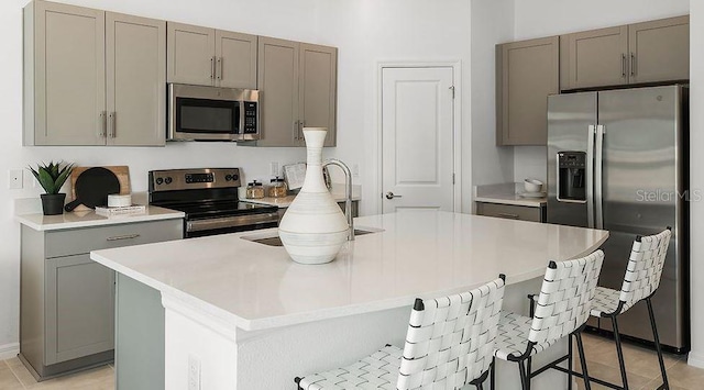 kitchen featuring gray cabinets, a kitchen bar, appliances with stainless steel finishes, light countertops, and light tile patterned floors