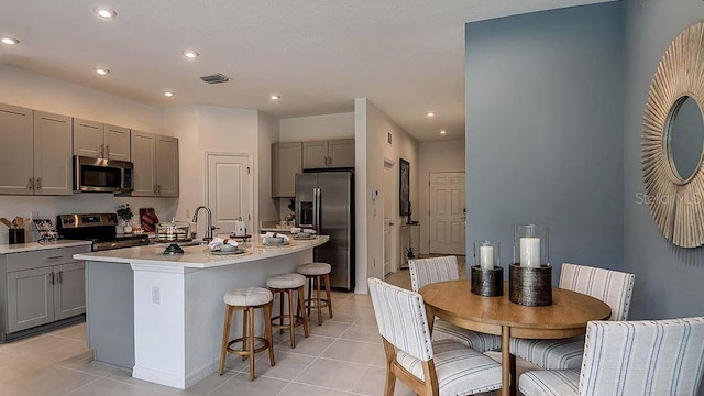 kitchen featuring stainless steel appliances, gray cabinetry, visible vents, and a kitchen bar