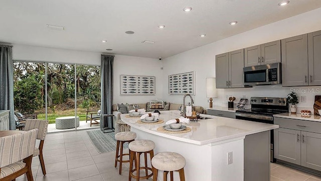 kitchen featuring a center island with sink, a sink, light tile patterned floors, gray cabinetry, and stainless steel appliances