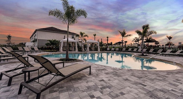 pool at dusk with fence, a community pool, a gazebo, and a patio area
