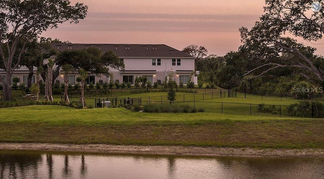 back of property featuring a lawn, a water view, and fence