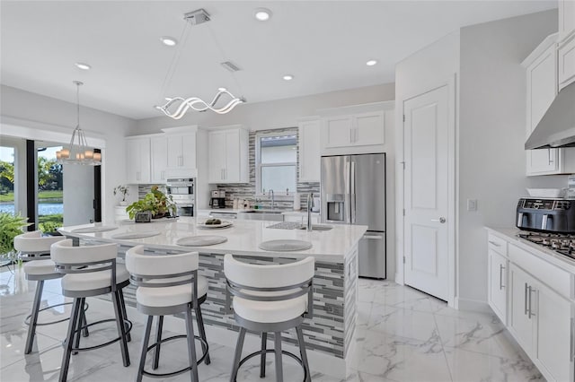 6203 Grandview Hill Ct, Bradenton, FL 34203 - kitchen featuring stainless steel appliances, a kitchen island with sink, white cabinetry, tasteful backsplash, and light marble finish floors