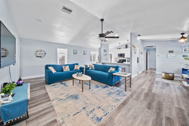 living area featuring ceiling fan, light wood finished floors, baseboards, lofted ceiling, and visible vents