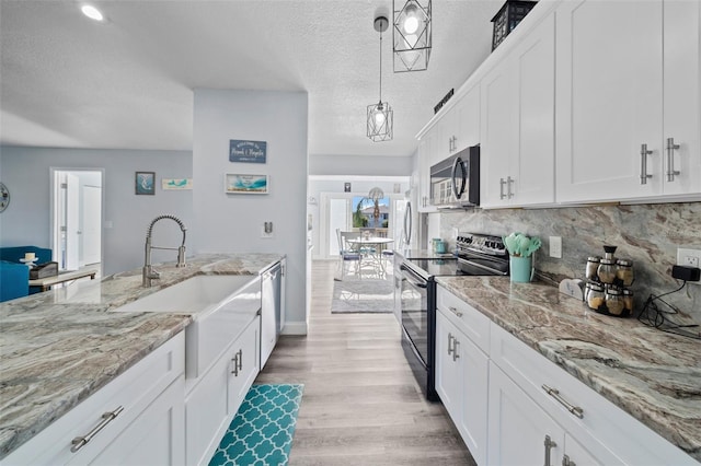 kitchen with white cabinets, a sink, light wood-style flooring, appliances with stainless steel finishes, and backsplash