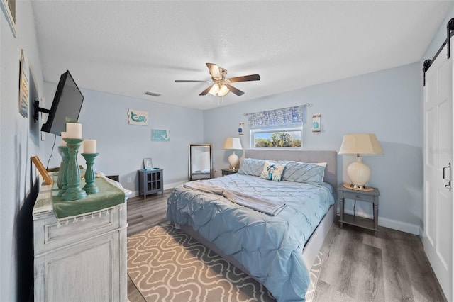 bedroom with visible vents, wood finished floors, baseboards, a barn door, and a ceiling fan
