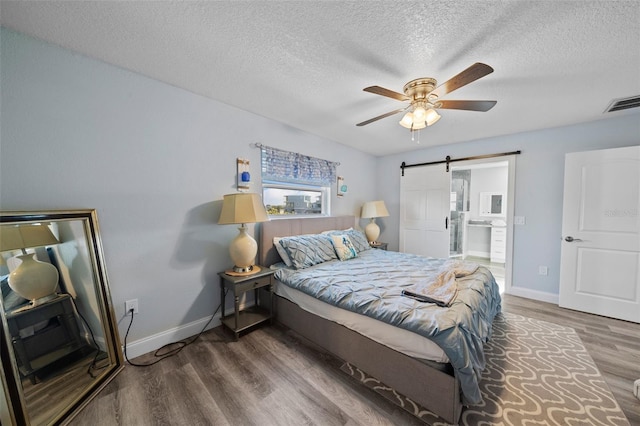 bedroom with a textured ceiling, visible vents, a barn door, and wood finished floors
