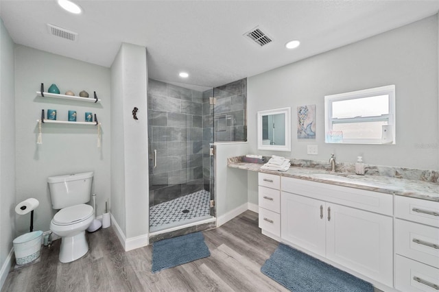 bathroom with a stall shower, toilet, wood finished floors, and visible vents